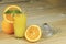 A hand squeezing juice from an orange on a manual glass squeezer. Set on a wooden planked table.