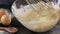 Hand stirring dough with a whisk in glass bowl.