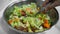 A hand stirring a fresh natural green salad in a bowl