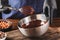 Hand stirring with a whisk melted dark chocolate in a metal bowl on a wooden table.