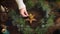 Hand in sweater lighting up candle in christmas wreath on rustic wooden table with pine cones, scissors and decorations. Candle in