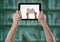 Hand with tablet showing hands with book against blurry bookshelf with green overlay