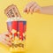 Hand takes a movie tickets and popcorn from a paper cup on a yellow background. Woman eats popcorn. Cinema Concept. Flat lay. Copy