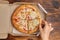 Hand takes piece of hawaiian pizza from cardboard packaging on wooden background