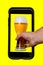 Hand is taking beer from phone on yellow background