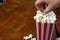 Hand taking popcorn out of red and white striped cardboard bucket retro design on wooden table