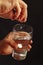 Hand throwing a soluble pill in a glass of water on dark background.