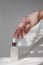 The hand touches a cosmetic bottle with essential oil or serum. White cosmetic bottle and female hand on a white background