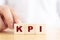 Hand touching wooden cube block with letter KPI is mean key performance indicator