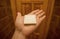 Hand of a tourist with piece of white soap form toiletries in a small hotel bathroom.