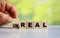 hand turns the wooden cube and changes the word UNREAL to REAL