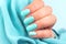 Hand with turquoise nails on blue textile background