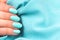 Hand with turquoise nails on blue textile background