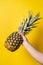 Hand of unknown woman holding pineapple - female hold fresh fruit on bright yellow background - healthy eating and diet modern