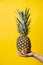 Hand of unknown woman holding pineapple - female hold fresh fruit on bright yellow background - healthy eating and diet modern