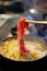 Hand using chopsticks to pick up raw sliced beef for eating Shabu Shabu or Japanese sukiyaki