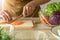 Hand is using knife cutting carrots and have a purple cauliflower cup in to next to it. The preparation for the vegetable salad