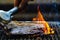 Hand using silver serving kitchen tongs holding raw meat beef steak bbq grilling on rack charcoal stove with smoke and fire flame