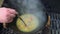 Hand using steel ladle to mix soup boiling in po on grill. Handheld shot.