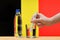 A hand with a water tester makes a measurement in a glass of clear water against the background of the flag of Belgium.