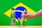 A hand with a water tester makes a measurement in a glass of clear water against the background of the flag of Brazil.