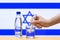 A hand with a water tester makes a measurement in a glass of clear water against the background of the flag of Israel.