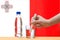 A hand with a water tester makes a measurement in a glass of clear water against the background of the flag of Malta.