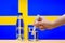 A hand with a water tester makes a measurement in a glass of clear water against the background of the flag of Sweden.