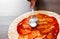 Hand woman cook with spoon smears tomato sauce on dough. making Italian pizza on wooden background