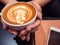 Hand woman holding a cup of hot latte arts coffee with cell phone and note on black table. Barista coffee art concept.with copy