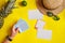 Hand of woman holding snapshot pictures. Straw hat, pineapple, lime, sunglasses and white sheets of paper on yellow