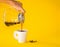 Hand woman pouring coffee on white paper cup with Roasted beans on yellow background