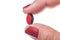 Hand of a woman with red nails holding a capsule pill close up isolated on white background.