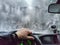 Hand of woman on steering wheel in car and and the forest with cloudy windshield, fogged with snow ice in winter