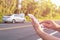 Hand of woman using smartphone and blur of her broken car parking on the road. Contacting car technician or need help concept