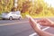 Hand of woman using smartphone and blur of her broken car parking on the road. Contacting car technician or need help concept