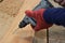 Hand of worker drills a hole with wooden plank using electric drill machine in workshop