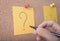 Hand writeing question mark on sticky note or post is on cork