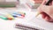 Hand writes with a black golden pen in a notebook on a white table with multi-colored school supplies for creativity and books