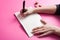 Hand writes in notebook and metal coin on pink background