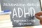 Hand writing on a blackboard in a class with the word ADHD written on. Some books and school materials.