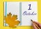 Hand writing the date 1 october in an open notebook with a beautiful natural maple leaf on a yellow background.