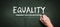 Hand is writing EQUALITY on a chalkboard