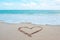 The hand writing heart shaped on the beach by the sea with white waves and blue sky