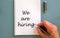 Hand writing `we are hiring` on white note, isolated on blue background