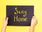 Hand writing Stay at home text on the black background. Two hands take the chalkboard on yellow background.