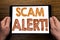 Hand writing text caption Scam Alert. Business concept for Fraud Warning Written on tablet laptop, wooden background with business