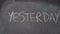 Hand writing `TODAY, YESTERDAY, TOMORROW` on black chalkboard