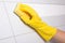 Hand in yellow glove cleaning tile wall