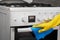 Hand in yellow glove cleaning white stove with blue rag